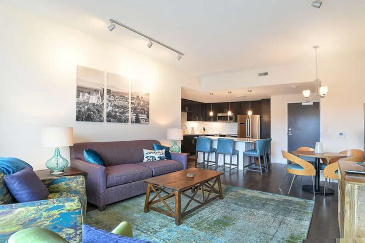 The image features a spacious, open-concept living area with a plush sofa, contemporary coffee table, stylish dining set, and a modern kitchen—all seamlessly connected for effortless entertaining and relaxation.