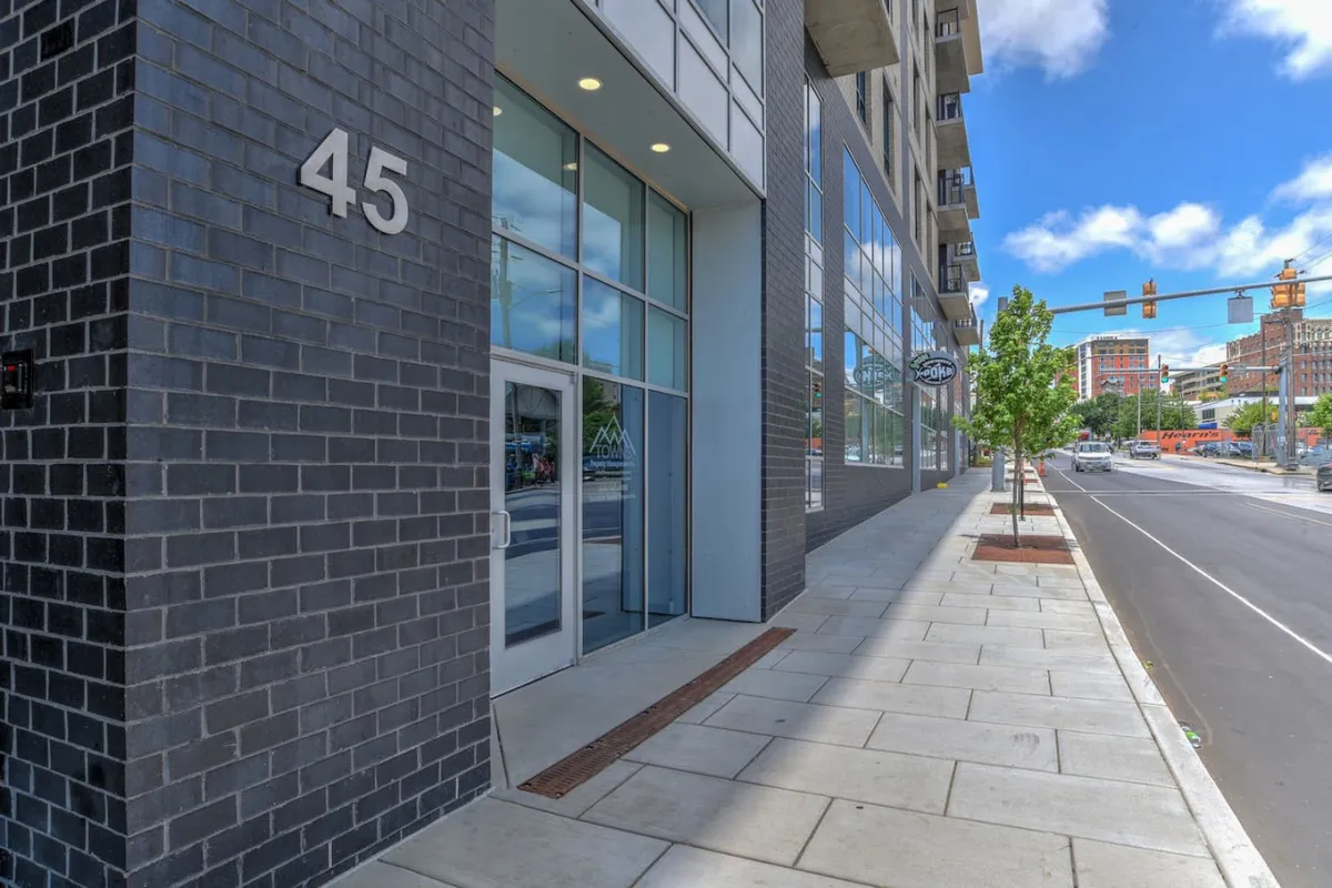This image displays the building’s secure entrance, featuring large glass windows and the prominent number '45' on the wall. The inviting sidewalk and street view signal easy, safe access, while the modern aesthetic sets the tone for exclusivity and peace of mind.