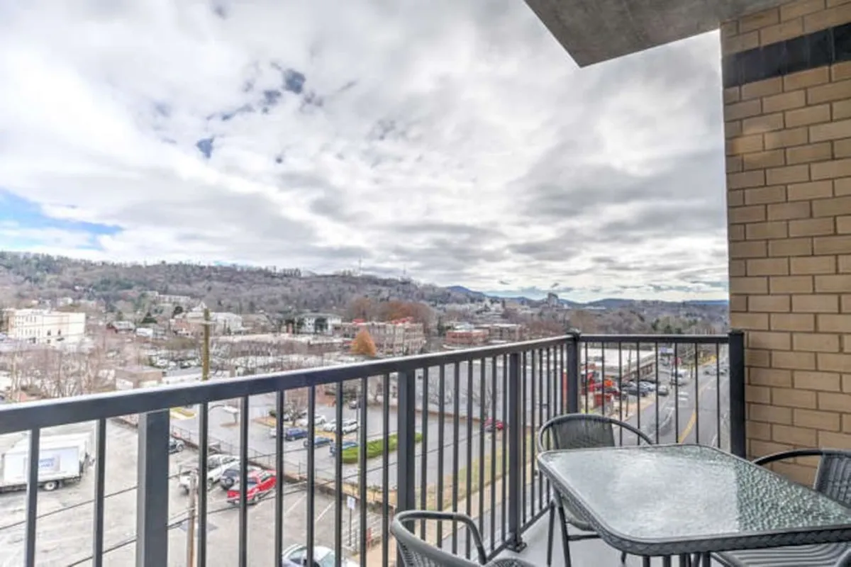 This image features a private balcony with a sleek railing, a table with chairs set for coffee or dining, and sweeping views of Asheville's cityscape with distant mountains. The tranquil atmosphere invites guests to relax, entertain, or simply enjoy the vibrant energy below from a peaceful, elevated perch.